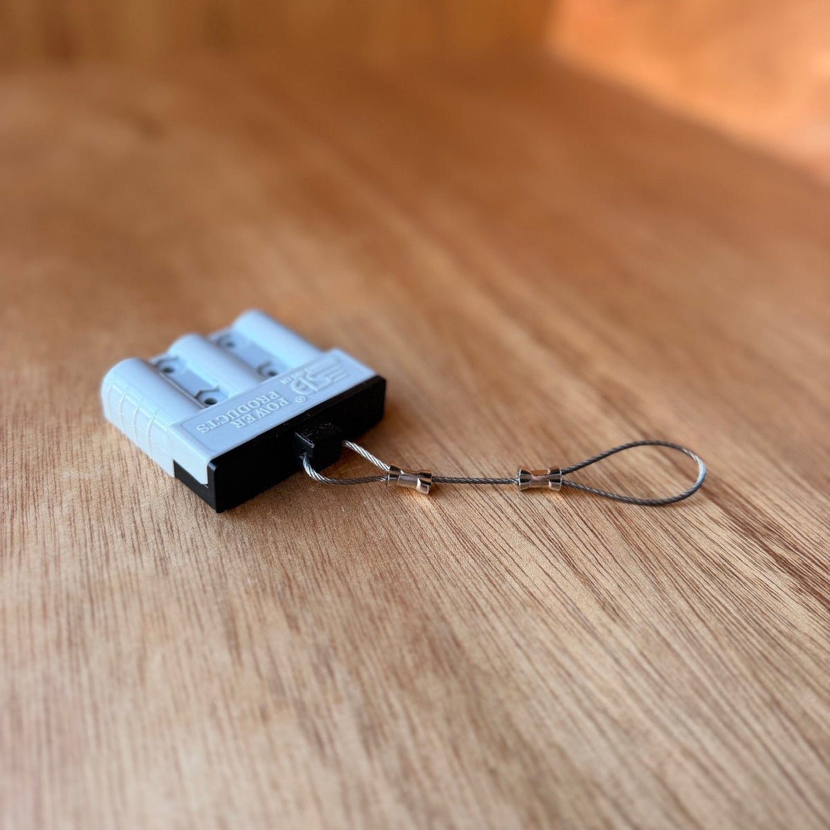 White Anderson-style plug fitted with a black TPU dust cover and stainless steel wire tether